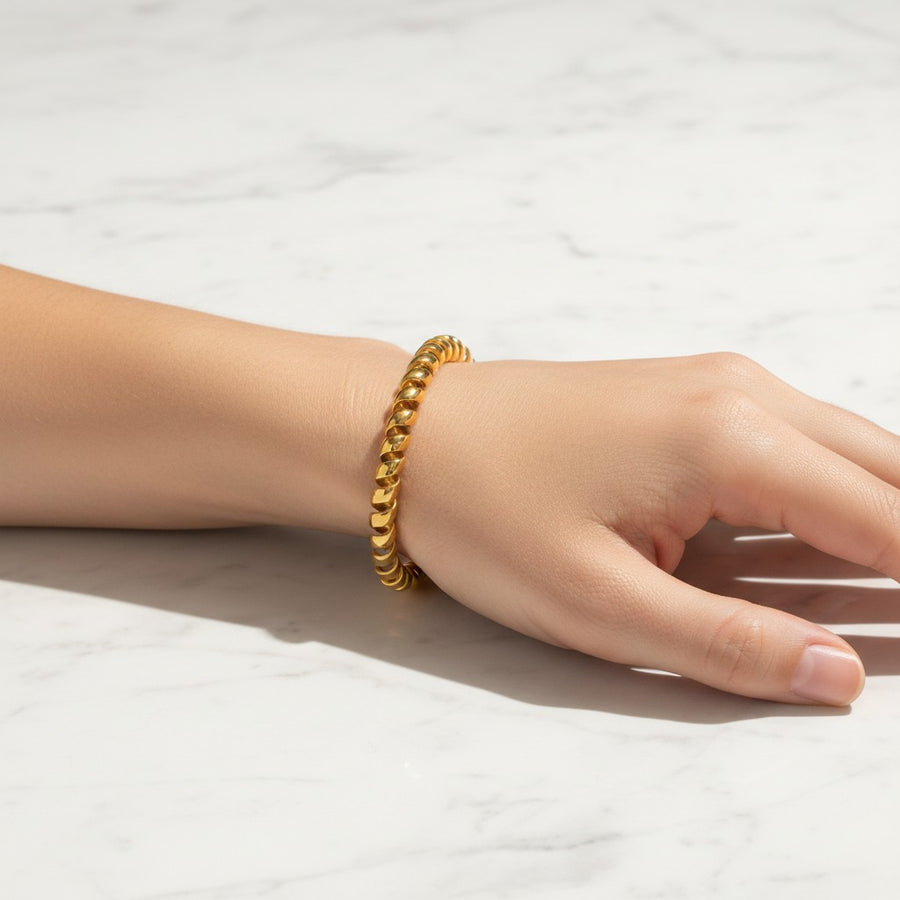 A gold beaded chain bracelet worn on a person's wrist, resting on a white marble surface.