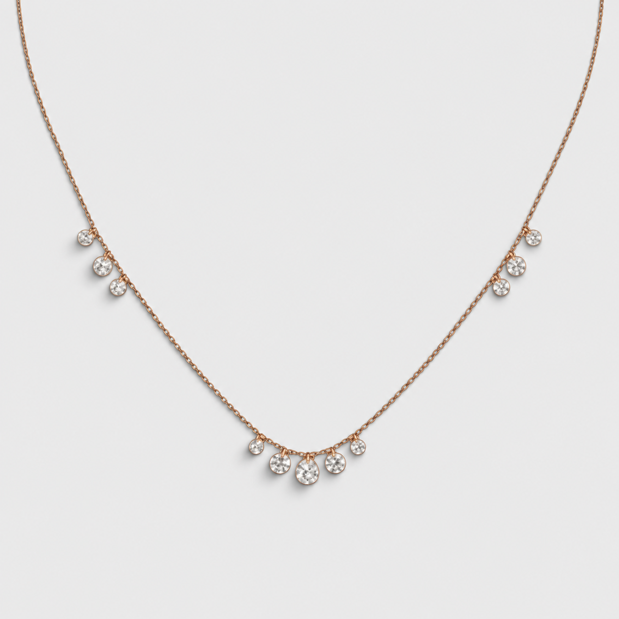 A delicate rose gold necklace featuring five small, clear crystal droplets spaced along the chain, displayed against a light gray background.