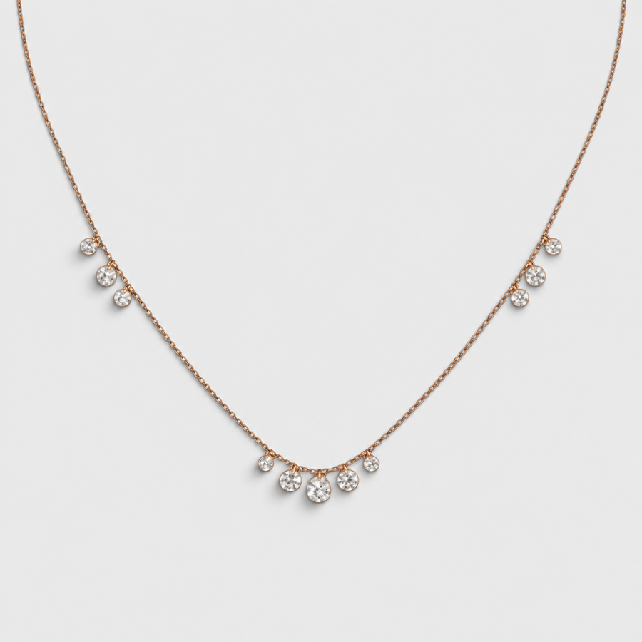A delicate rose gold necklace featuring five small, clear crystal droplets spaced along the chain, displayed against a light gray background.