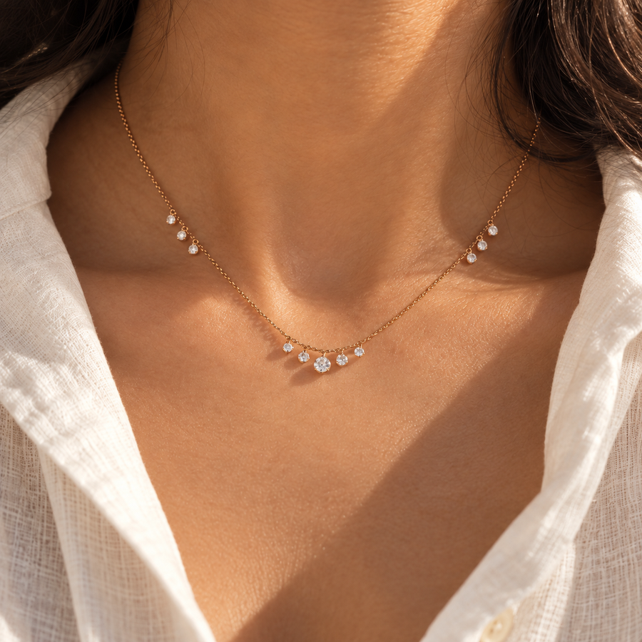 A delicate gold chain necklace with small clear gemstones worn on a model's neck, paired with a white linen shirt.