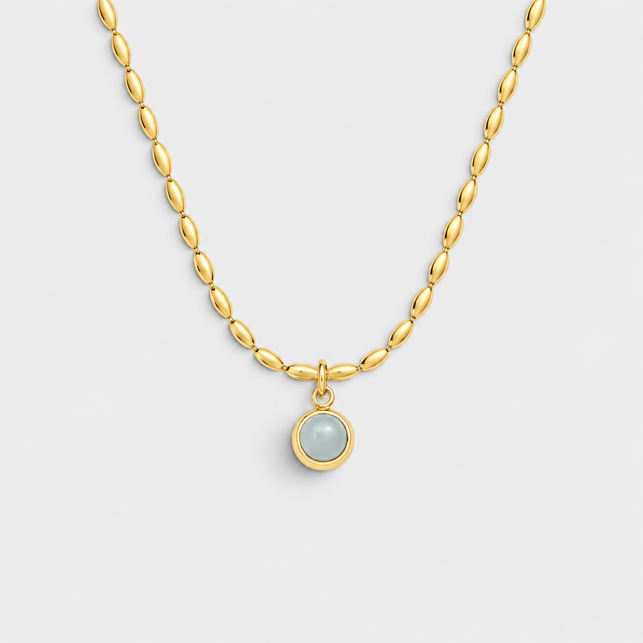 A gold chain necklace with a small oval pendant featuring a pale blue-gray stone in a gold bezel setting, shown on a light gray background.
