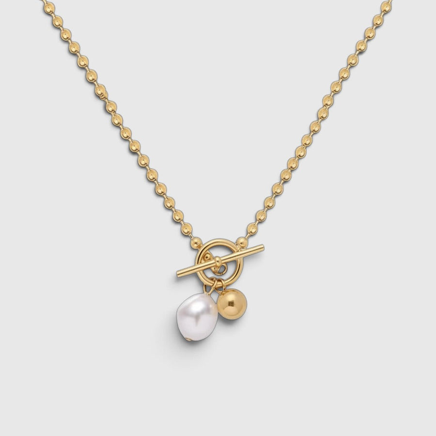 A gold necklace with a beaded chain, toggle clasp, and a dangling white pearl and gold bead charm, shown on a light gray background.