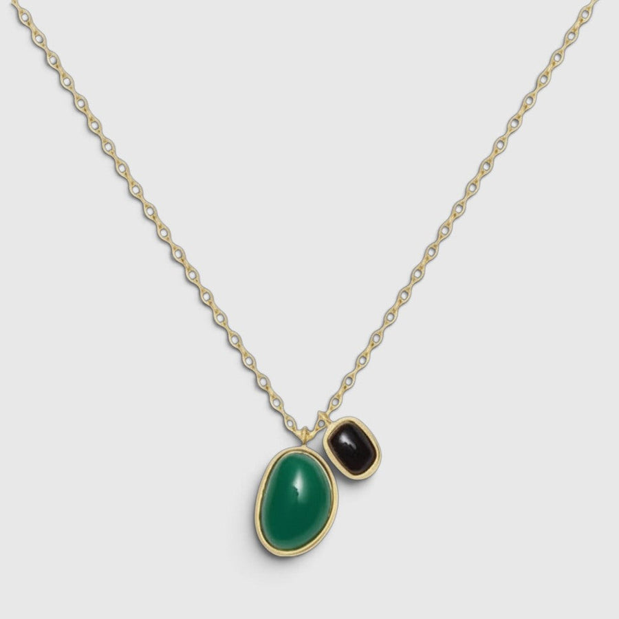 A gold chain necklace featuring a large, smooth green teardrop-shaped stone and a smaller, polished black stone, both set in gold bezels, shown against a light gray background.