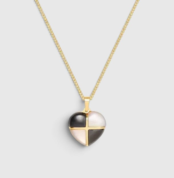 A gold chain necklace with a heart-shaped pendant featuring a black and pale pink enamel design divided by a gold cross, shown on a light gray background.