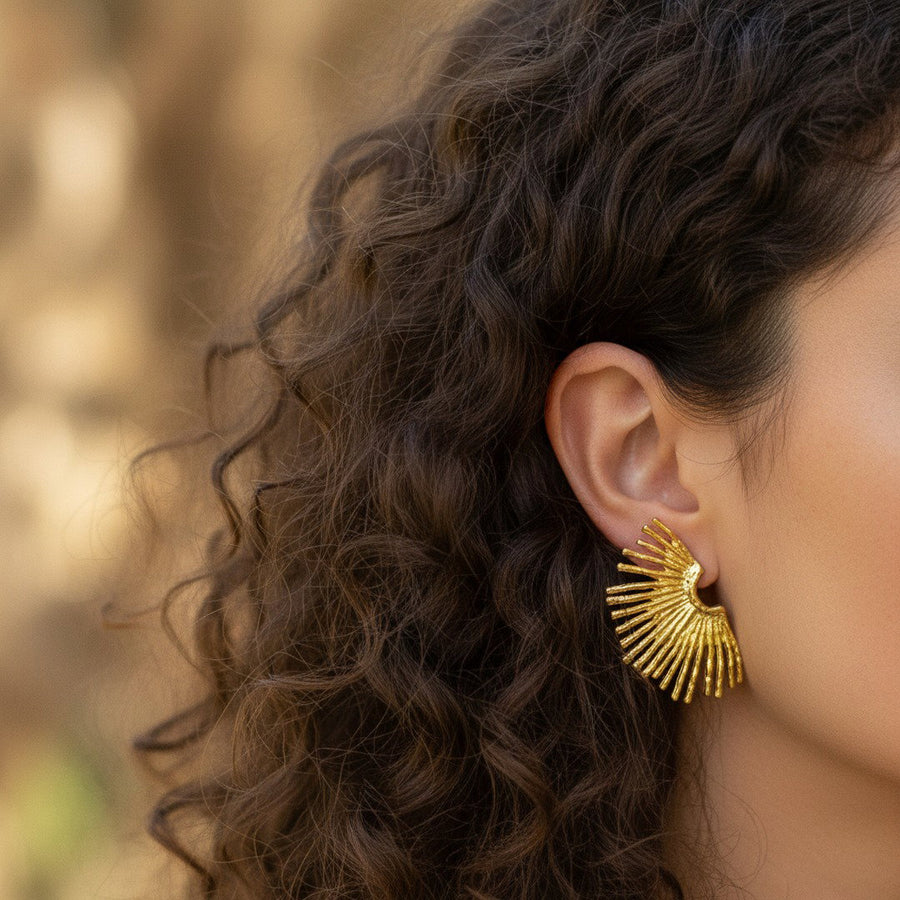 Close-up of a person wearing a gold earring with a blurred natural background